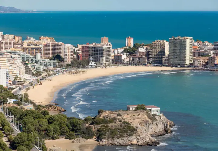 Vista panorámica de la **playa de la Concha Oropesa**, con edificios residenciales, el mar azul y una costa rocosa.