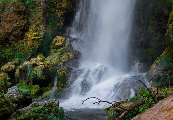 Cascada con rocas cubiertas de musgo y vegetación exuberante.