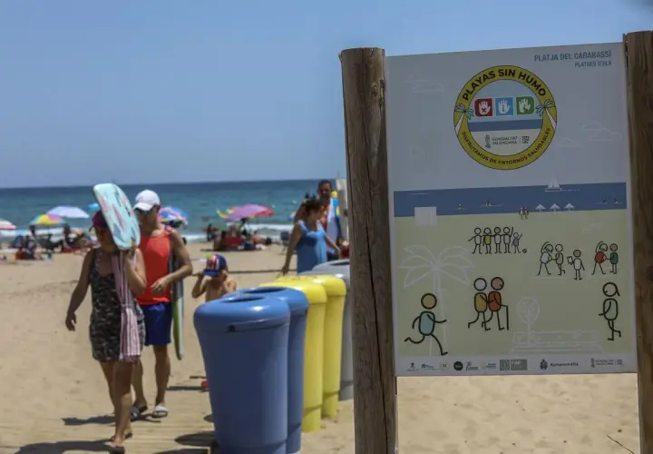 Cartel en la playa de El Carabassí, Alicante, indica "Playas sin humo". Familias disfrutan del sol y el mar.