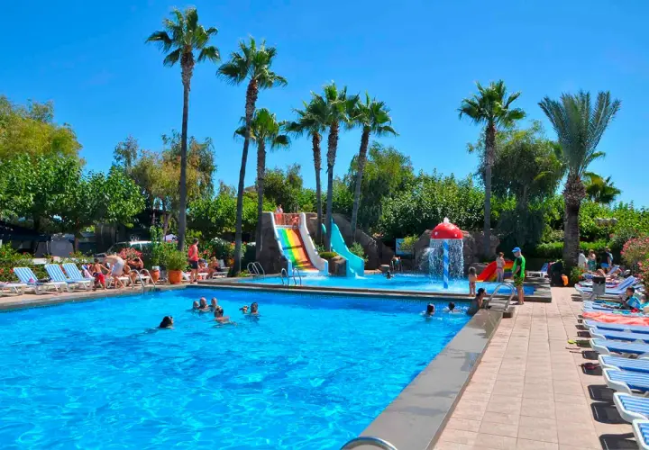 ¡Un día bravo en la playa! Niños y adultos disfrutan de toboganes acuáticos y una piscina refrescante bajo palmeras.