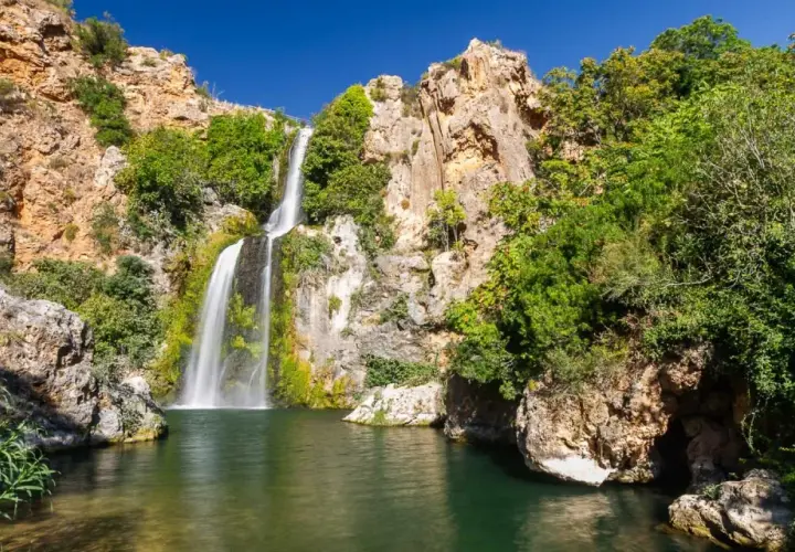 El Salto de Chella, una cascada imponente rodeada de rocas y vegetación exuberante, cae en una poza de agua verde.