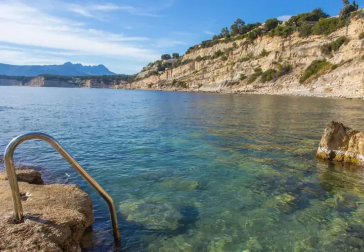 Escalera metálica para acceder a las aguas cristalinas de cala Punta Estrella, con acantilados y montañas al fondo.