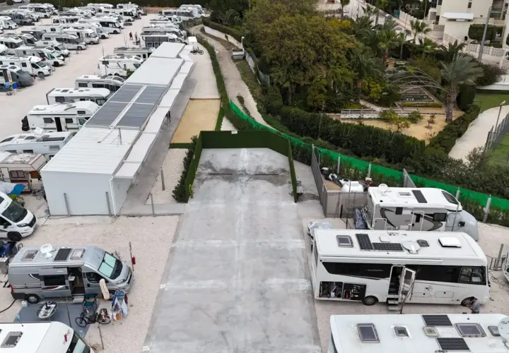Amplio camper park en Alicante con numerosas autocaravanas y caravanas aparcadas, algunas con paneles solares.