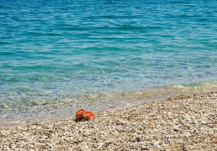 Chanclas naranjas abandonadas en la **playa Malvarrosa de Corinto**, esperando a su dueño junto a las aguas cristalinas.