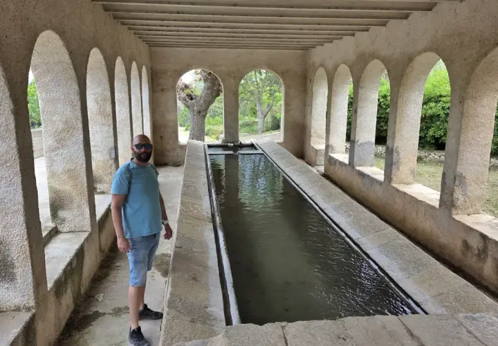 Un hombre posa junto a una larga pila de agua, un lugar que parece la "catedral del senderismo" por su arquitectura y entorno natural.