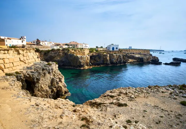 Explora la isla de Tabarca: casas blancas sobre acantilados rocosos, aguas cristalinas y barcos en el horizonte. Un lugar para descubrir.