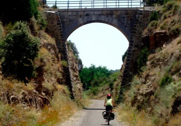Ciclista pedalea por la vía verde Valencia bajo un antiguo puente de piedra.