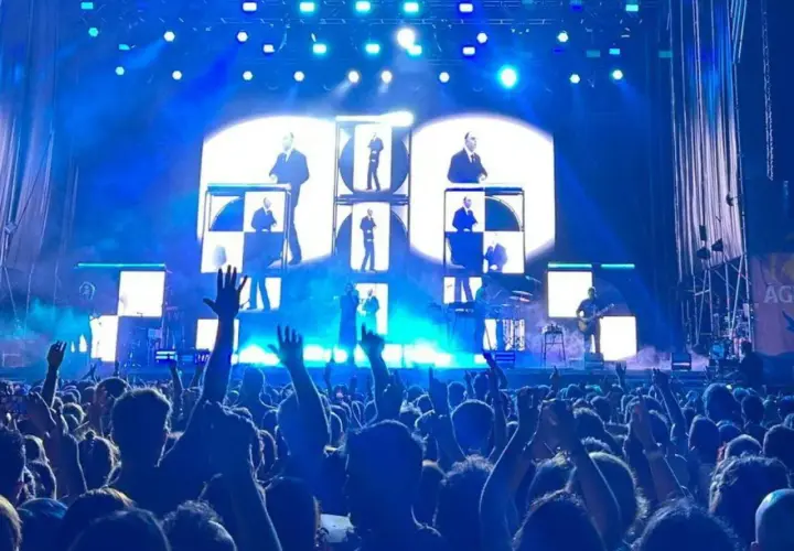 Multitud en concierto de Vetusta Morla en Valencia. Luces azules y pantallas con imágenes de los miembros de la banda crean un ambiente electrizante.