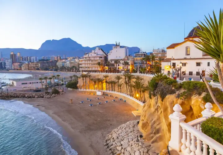 Atardecer en la playa Poniente de Benidorm, con el mar azul, la arena dorada, palmeras y edificios modernos.