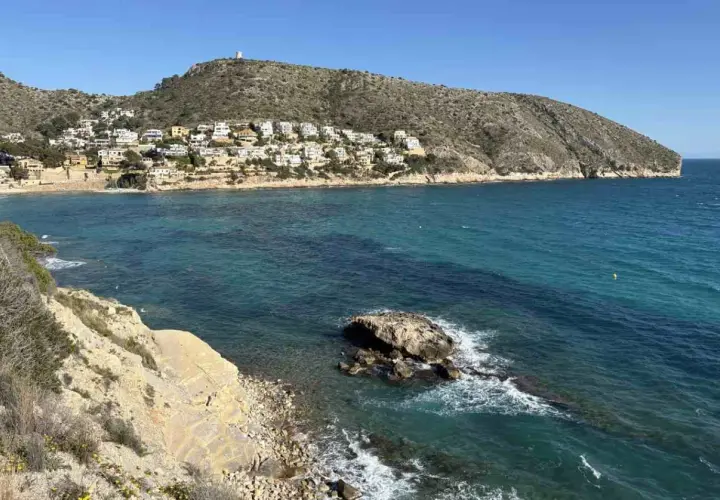 Vista de calas y acantilados con casas blancas en la ladera, aguas turquesas y un peñasco en el mar. Playas bonitas cerca de Benidorm.