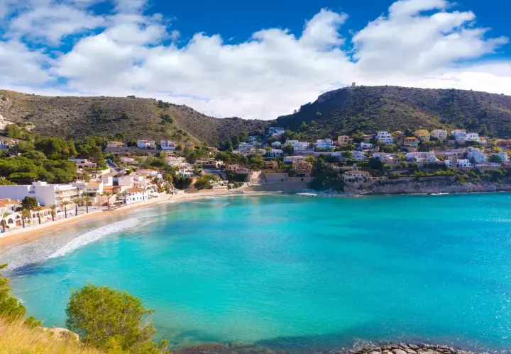 Bahía de aguas turquesas en cala el Portet, con casas blancas y verdes colinas.