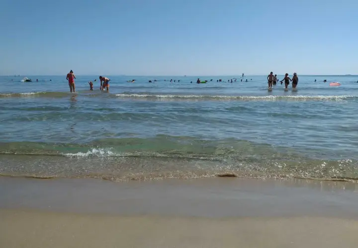 Gente disfrutando del mar y la arena en les palmeretes. El agua cristalina y el cielo azul invitan a un día perfecto.