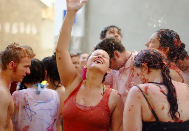 Gente feliz y empapada de tomate en la Tomatina, con una mujer riendo a carcajadas y el brazo en alto.