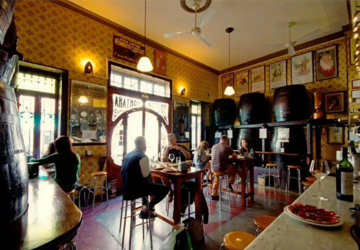 Gente en un bar tradicional, con barriles y carteles antiguos. Un lugar con encanto, como una casa de montaña en Valencia, donde disfrutar de tapas y vermut.