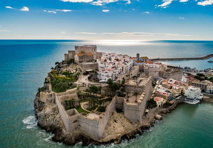 Castillo de Peñíscola sobre el mar, con sus murallas y casas blancas. La peñíscola playa se extiende a su lado, invitando a disfrutar del sol y el Mediterráneo.