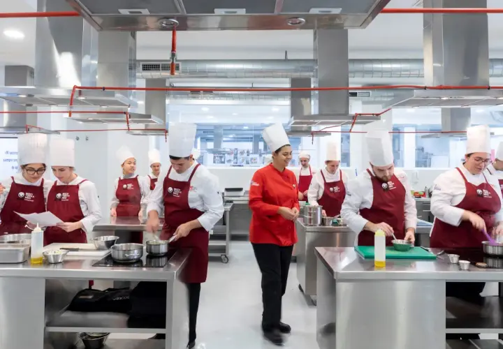 Estudiantes en un centro culinario mediterráneo, con toques rojos y blancos, aprendiendo a cocinar.