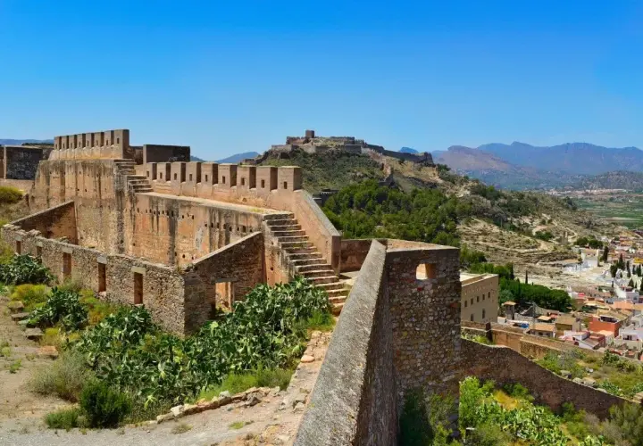 Ruinas del castillo de Sagunto, con sus imponentes murallas de piedra y escalinatas, dominan el paisaje montañoso.