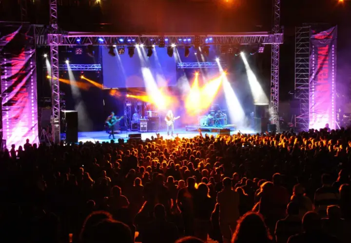 Multitud disfrutando de un concierto en un som festival, con luces brillantes y músicos en el escenario.