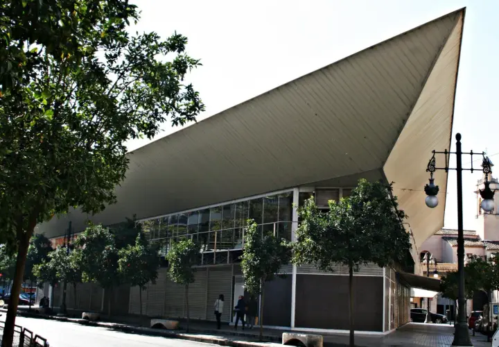 Edificio moderno con techo triangular y árboles en la calle frente al mercado de Jesús.