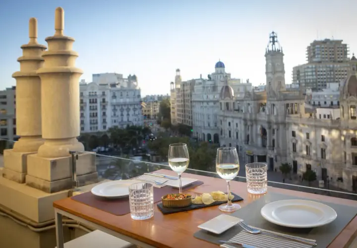 Una mesa en una terraza con vistas a la ciudad, con copas de vino y aperitivos, bajo el cielo de Atenea.