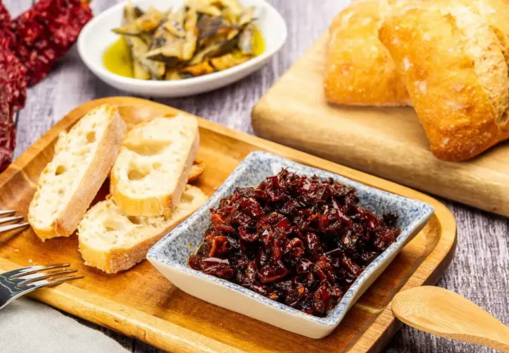 Pericana receta: pan rústico, pimientos secos y un cuenco con la deliciosa pericana, lista para untar.