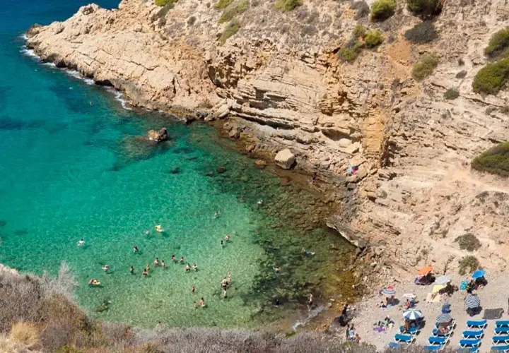 Aguas cristalinas y gente disfrutando en una cala rocosa, un paraíso que recuerda a las mejores calas de Benidorm.