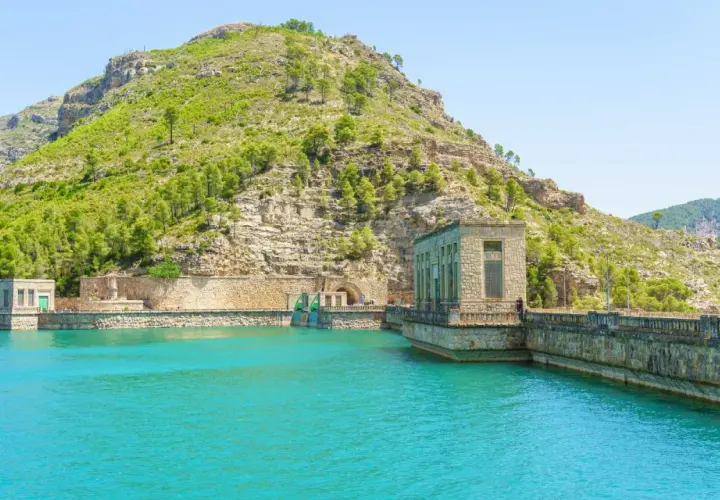 El embalse de Benagéber, con sus aguas turquesas y la imponente presa de piedra, se funde con la montaña verde.
