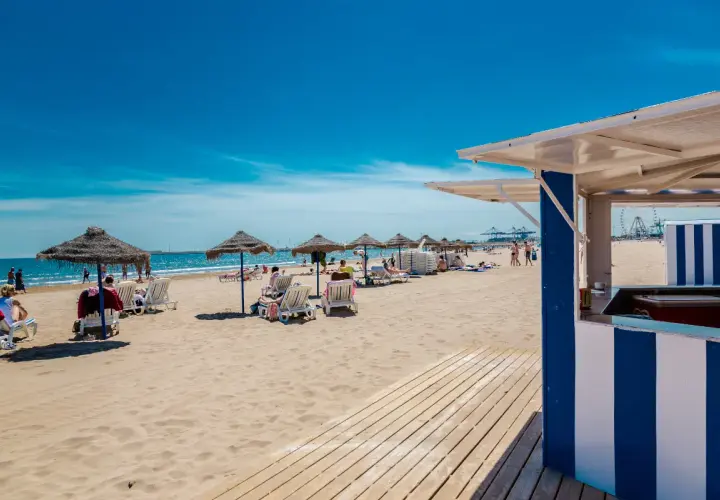 Día soleado en la strand Valencia. Sombrillas, tumbonas y gente disfrutando de la arena dorada y el mar azul.