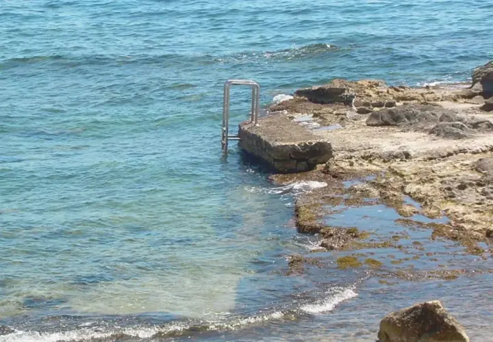 Escalera metálica en una roca que se adentra en el mar azul de cala l'andragó.