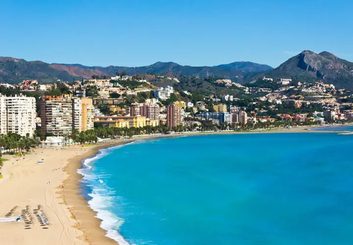 Vista panorámica de zonas de Alicante con playa, edificios altos y montañas al fondo.