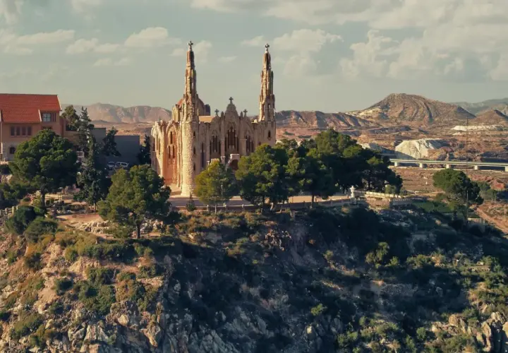 El **santuario** de Novelda se alza majestuoso sobre una colina, rodeado de vegetación y con un paisaje árido de fondo.