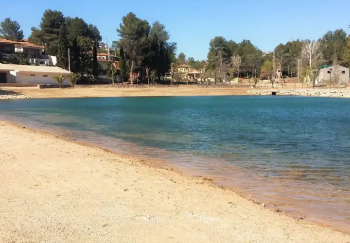 Arena dorada y aguas turquesas en la playa de Monte Navarrés, rodeada de pinos y casas.