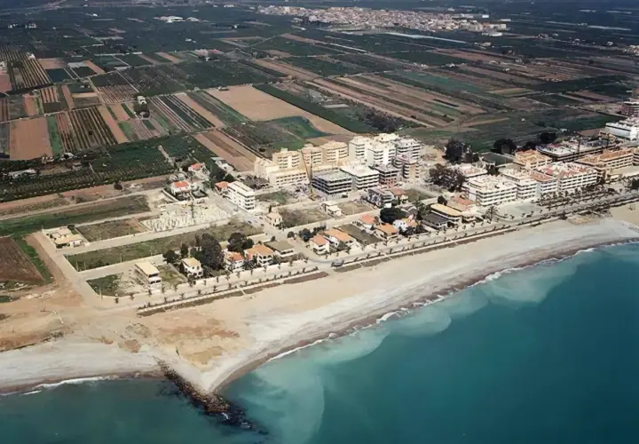 Vista aérea de la costa de Moncofa, con edificios residenciales y campos agrícolas. La playa de Moncofa se extiende hacia el mar turquesa.