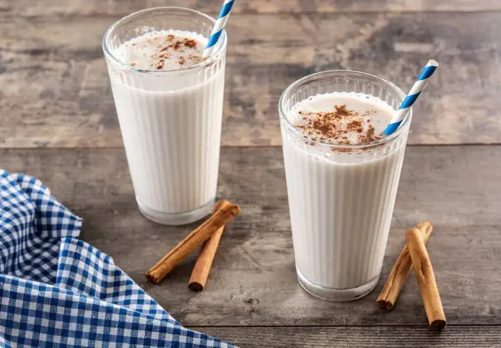 Dos vasos de horchata, bebida refrescante de chufa con canela, sobre mesa de madera.
