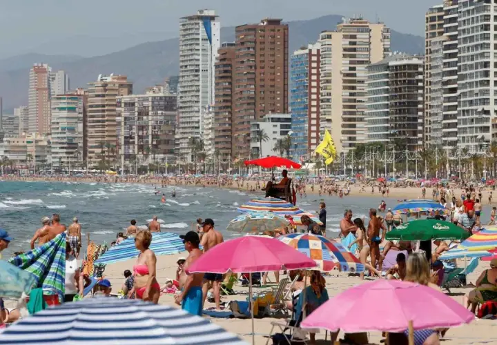 Gente disfrutando de un día soleado en la mejor playa de Benidorm, con edificios altos de fondo y sombrillas de colores.