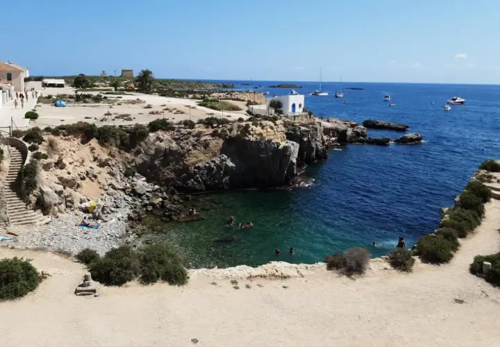 Gente nadando y tomando el sol en las calas de la isla Tabarca, con aguas cristalinas y barcos en el horizonte.