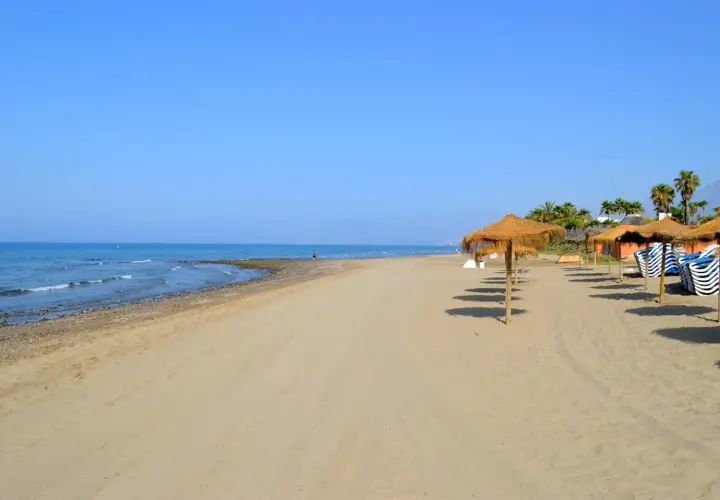 Arena dorada y mar azul en la playa de Alicante, con sombrillas de paja y tumbonas listas para disfrutar del sol.