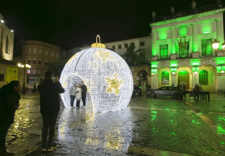 Una gran bola de luces ilumina la plaza en esta nit de cap d'any. Gente se hace fotos junto a la decoración.