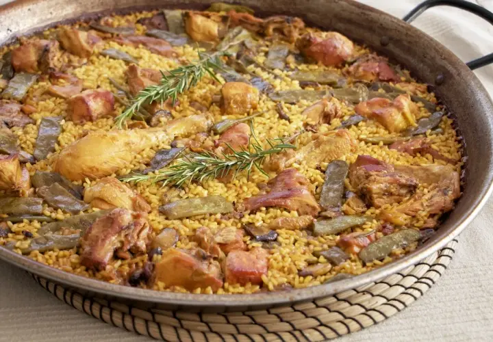 Paella valenciana recién hecha, con arroz amarillo, trozos de pollo, judías verdes y romero fresco.