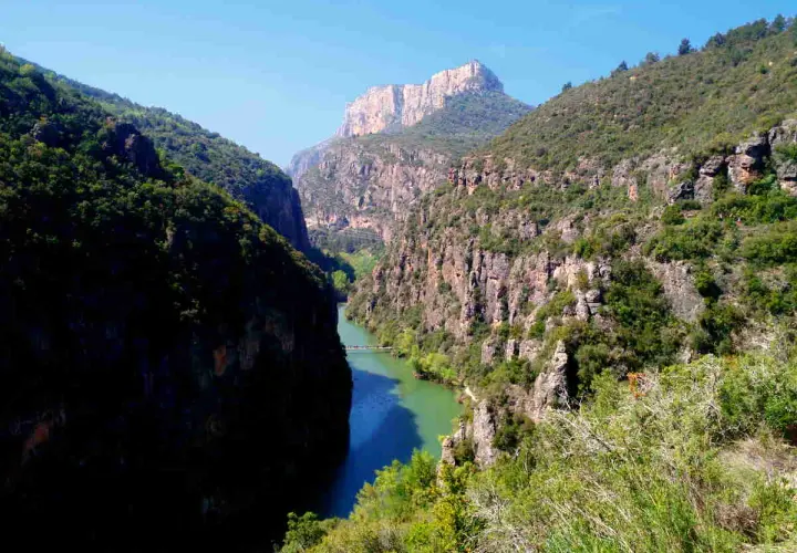 Impresionante desfiladero de Mont-rebei, con un río de aguas turquesas serpenteando entre imponentes paredes rocosas cubiertas de vegetación.