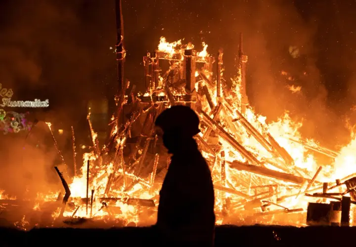 Silueta de persona observando la **cremà** de una falla en **Valencia**. El fuego consume la estructura de madera, creando un espectáculo de llamas y humo.