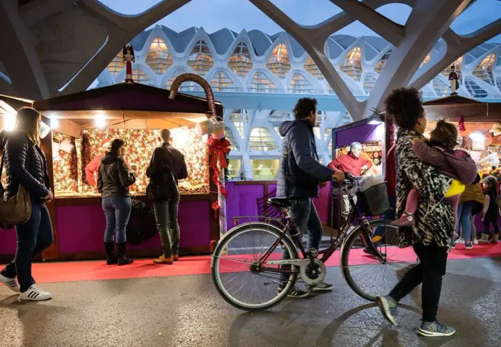 Gente pasea por puestos del **Valencia Christmas Market** bajo una estructura futurista.