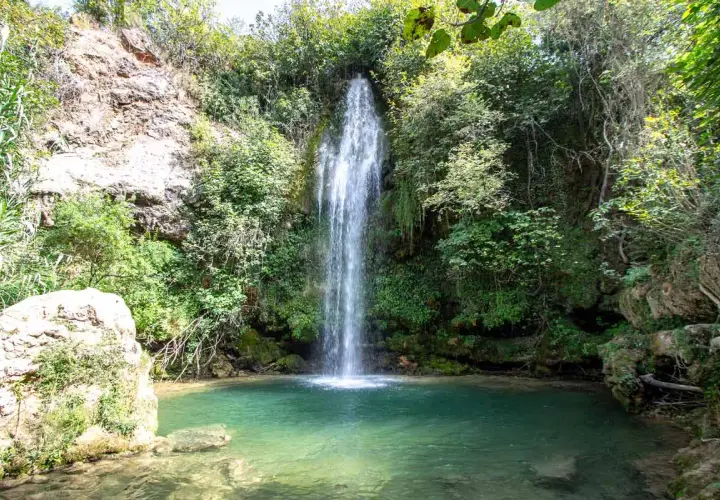 Los chorradores de Navarres, una cascada cae en una poza de agua turquesa rodeada de vegetación exuberante y rocas.