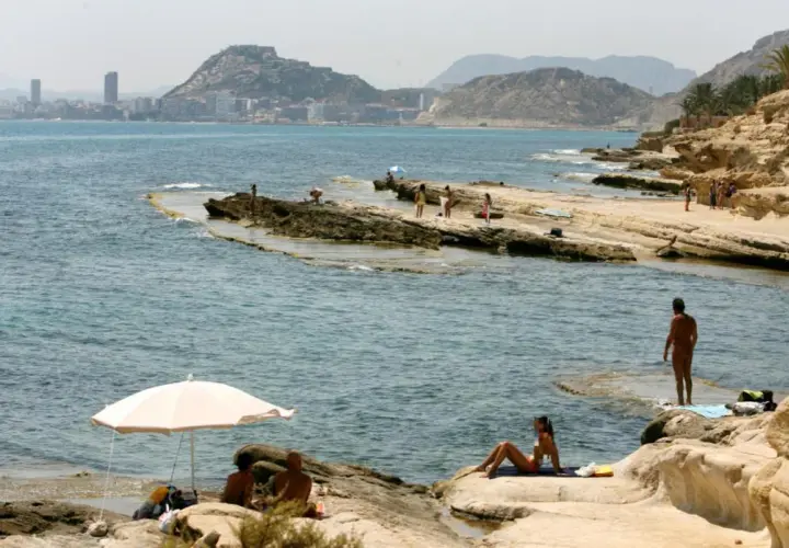 Gente disfrutando del sol y el mar en las playas nudistas de Calpe, con la ciudad al fondo.