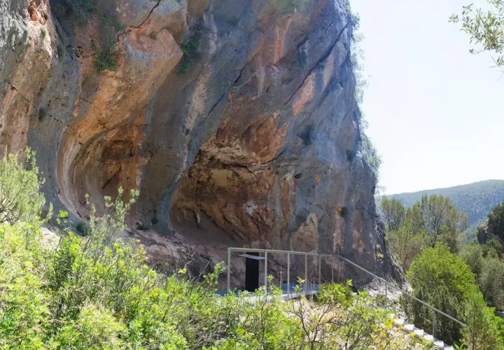 La cueva de la araña, una entrada moderna a una formación rocosa natural, se asoma entre la vegetación.