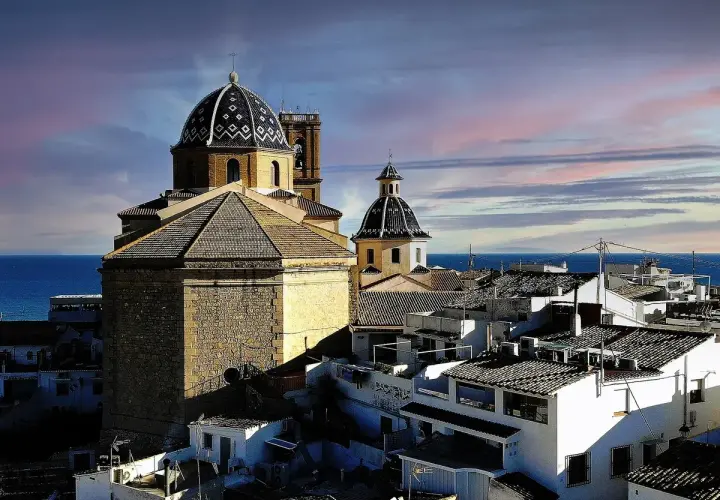Altea vieille ville, con sus cúpulas y tejados blancos, se asoma al mar Mediterráneo bajo un cielo teñido de rosa y azul.