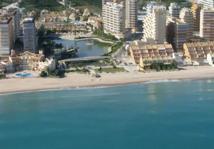 Vista aérea de la playa de la goleta, con edificios residenciales, una laguna artificial y el mar turquesa.