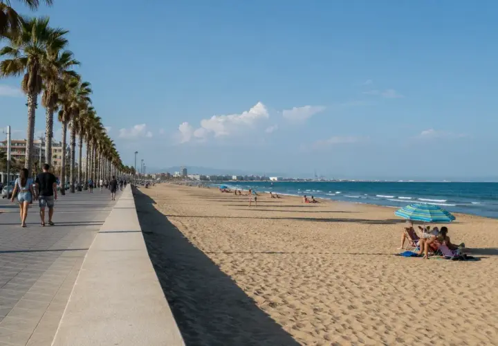 Paseo marítimo con palmeras y gente disfrutando de las **plages valence** bajo un cielo azul.