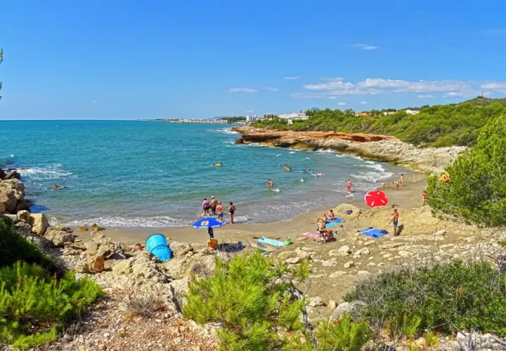 Gente disfrutando del sol y el mar en la cala blanca de Castellón, con aguas turquesas y vegetación mediterránea.