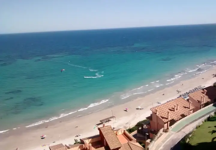 Vista aérea de la Campoamor playa con aguas turquesas, gente disfrutando del sol y un kitesurfista en acción.